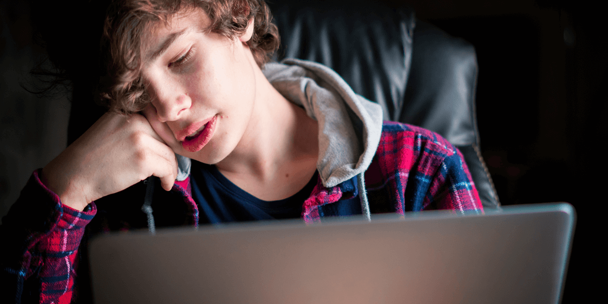 Teenage boy in front of a computer screen, resting head on hand