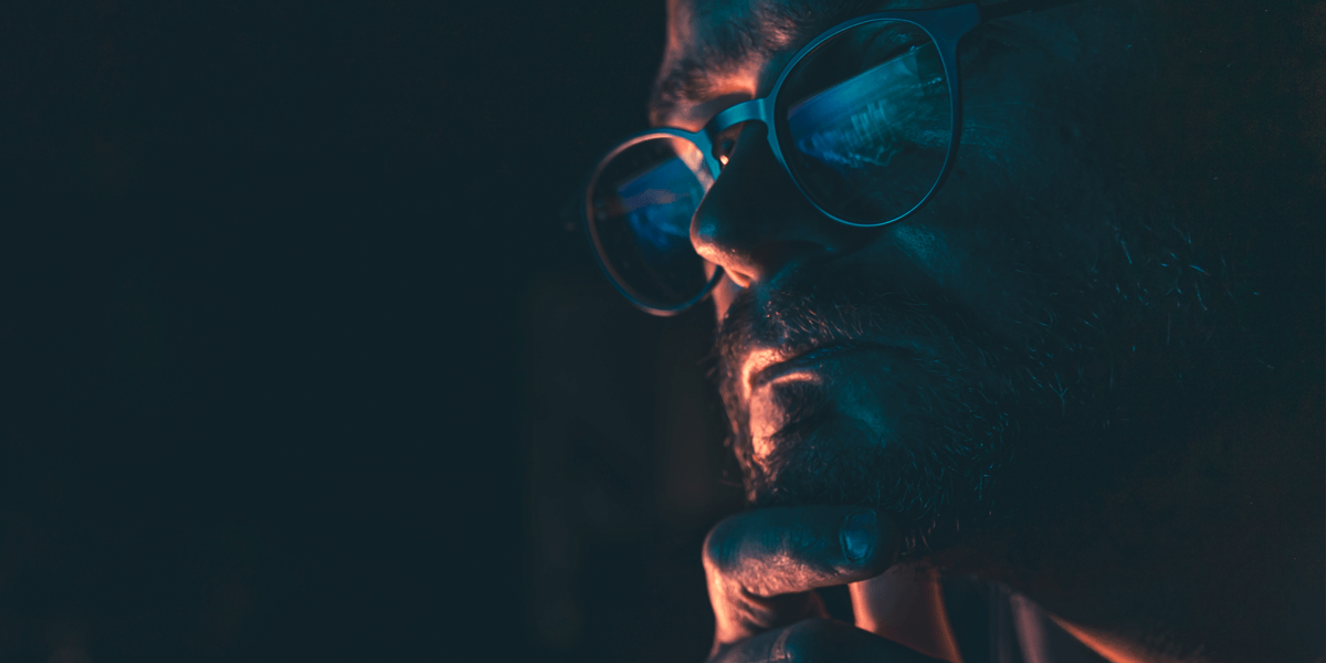 Half-shadowed face of a man with screen reflected in his glasses