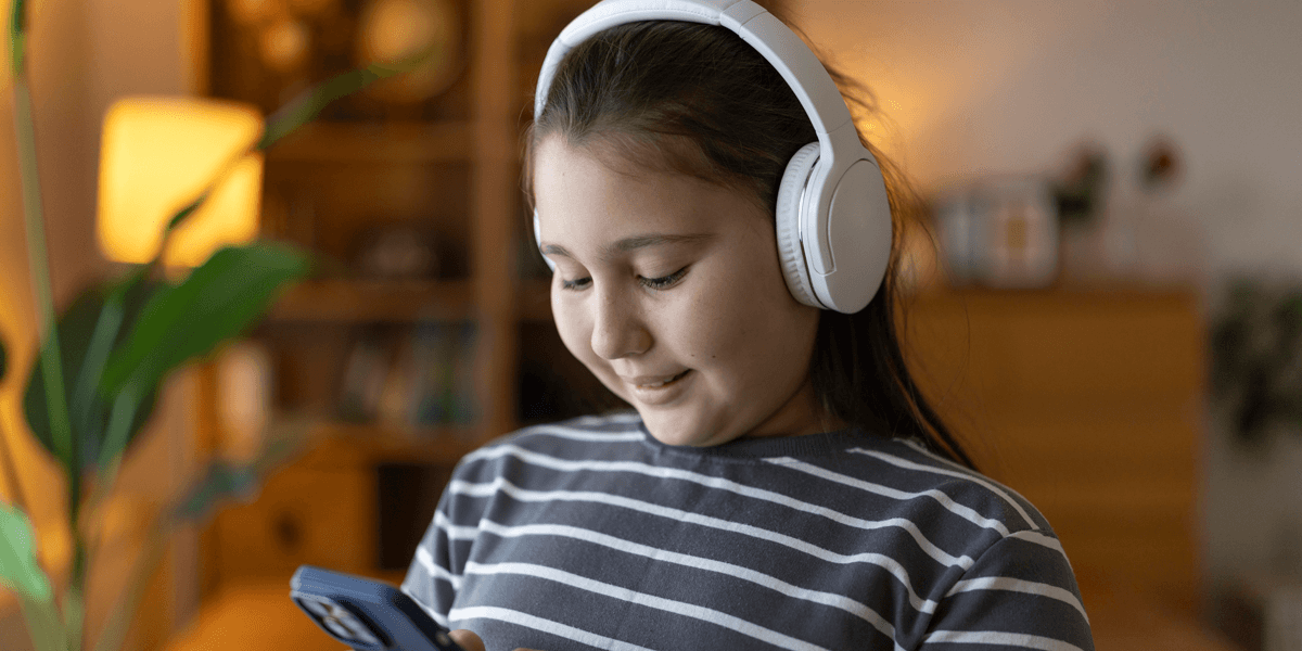 preteen girl wearing white headphones smiles at her phone
