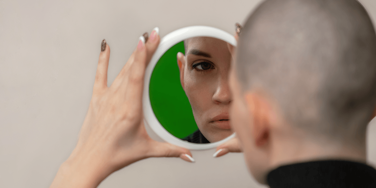 Woman with shaved head looks in a mirror