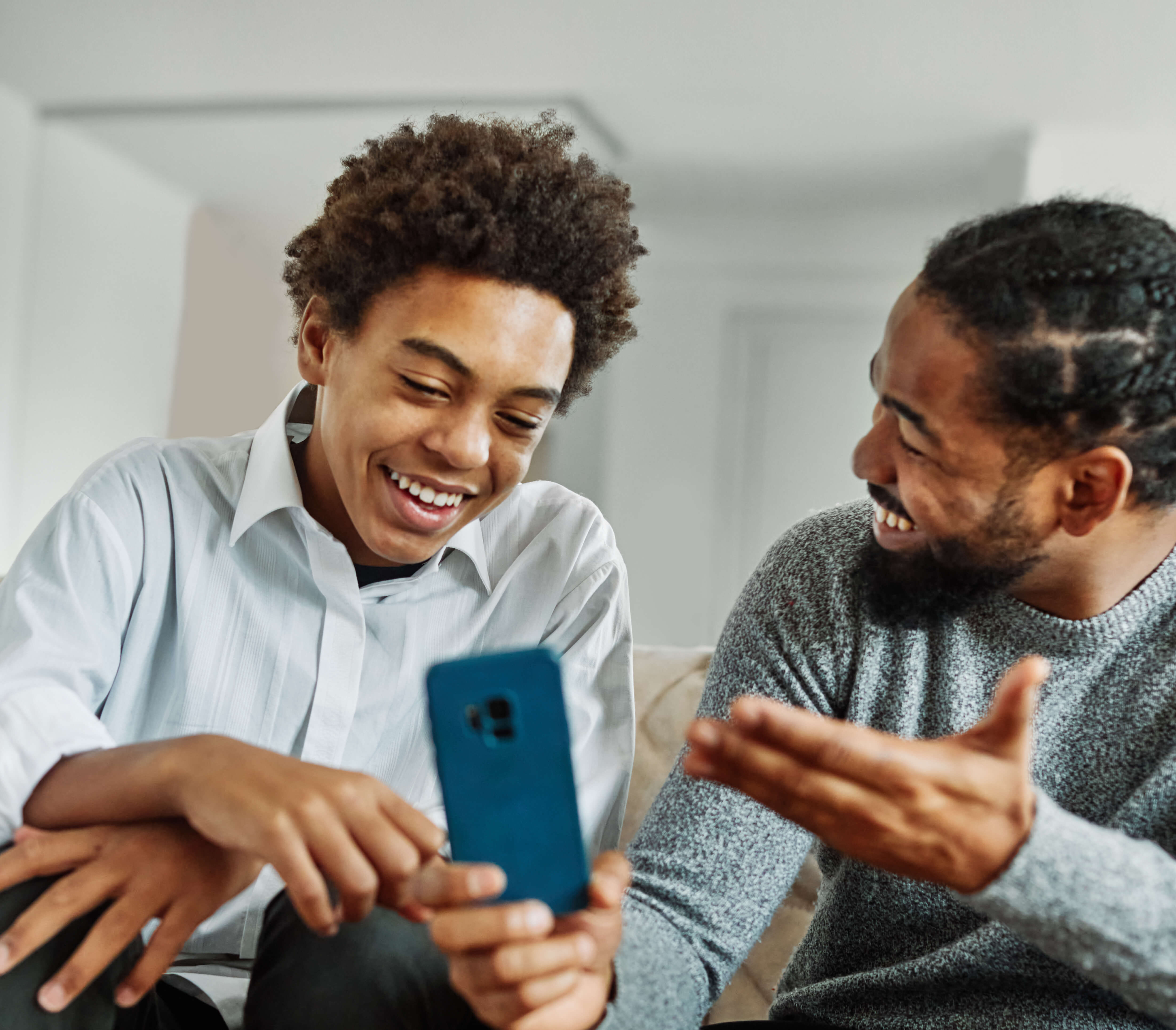 A teen and an adult laughing at something on a phone